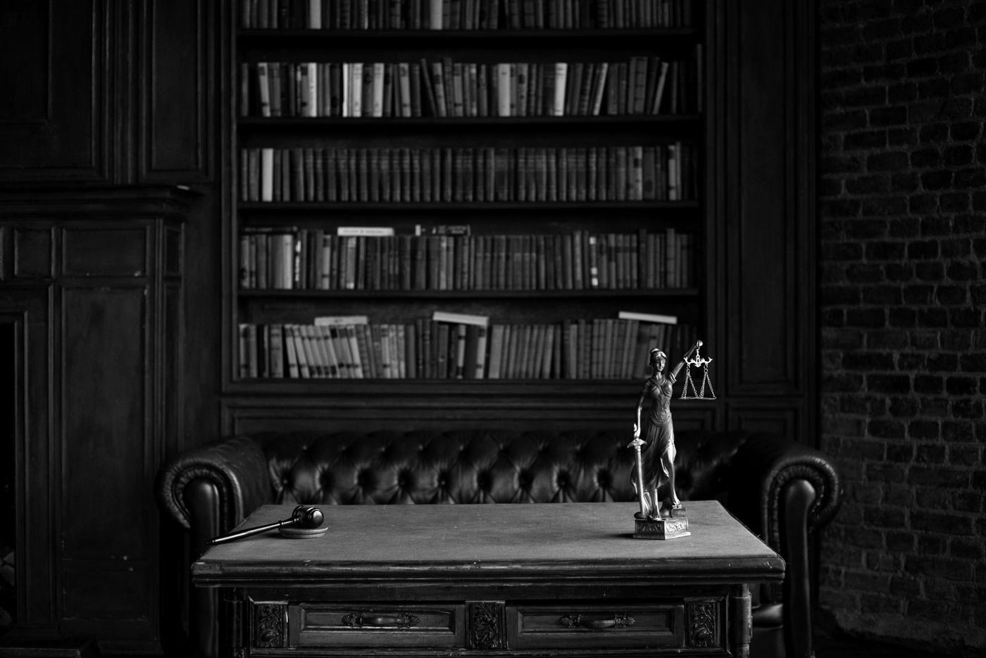 Sala de estudo antiga com estantes de livros e uma estátua da justiça sobre a mesa, em preto e branco