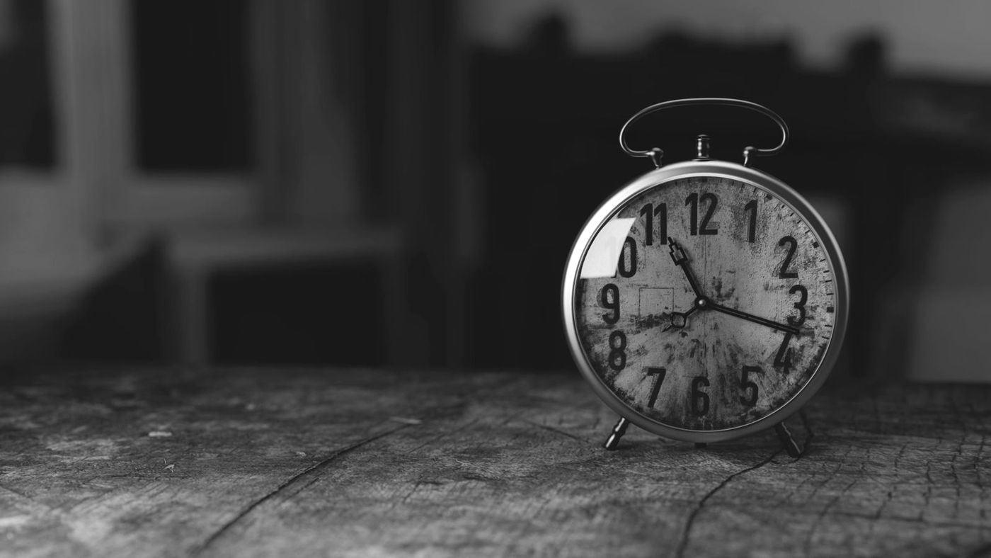 Relógio despertador antigo sobre uma mesa de madeira, em preto e branco