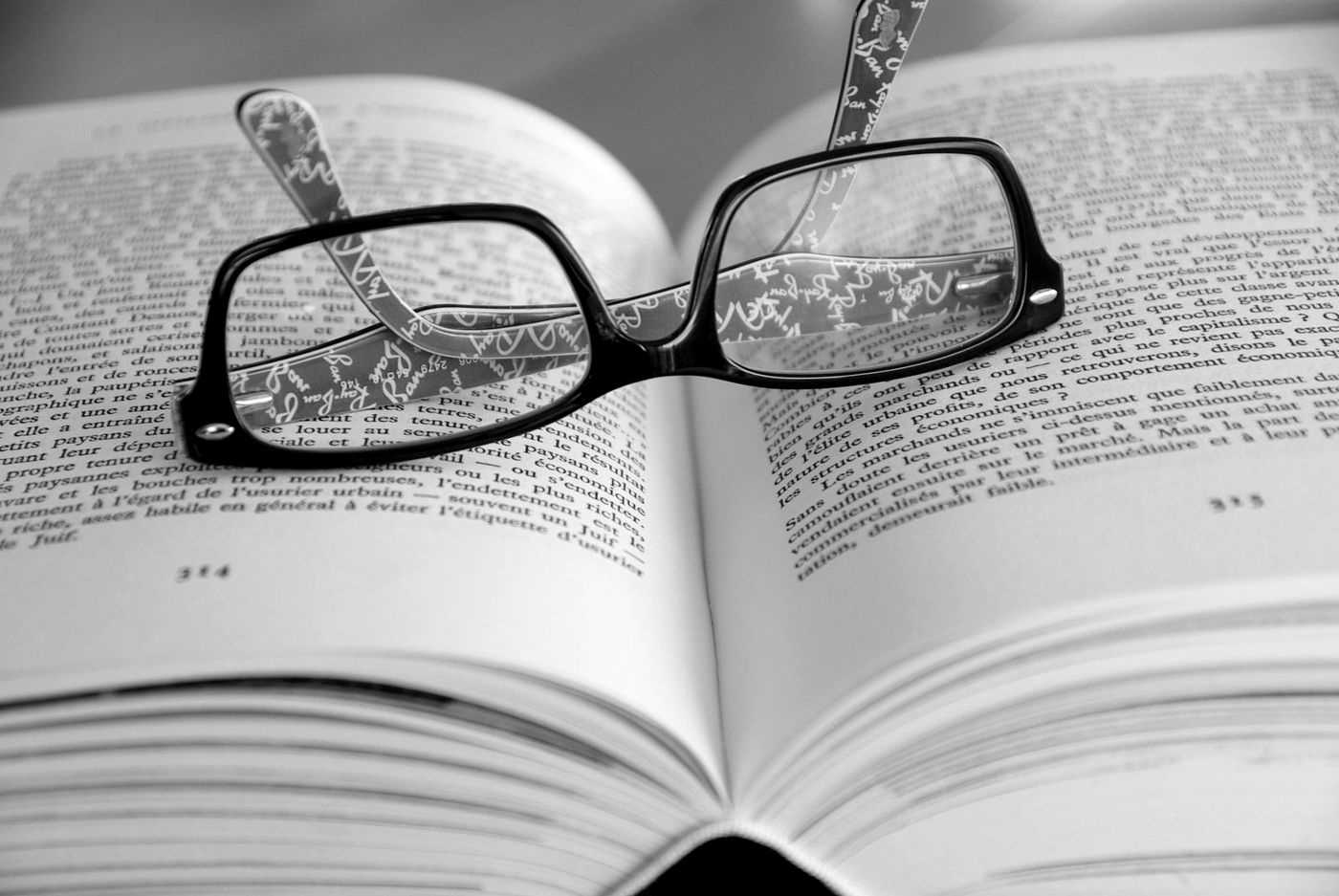 Óculos sobre as páginas de um livro aberto, em preto e branco