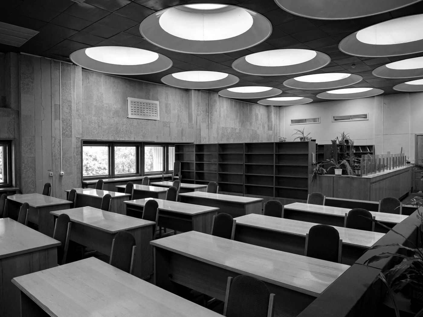 Sala de leitura vazia de uma biblioteca, com mesas enfileiradas, em preto e branco