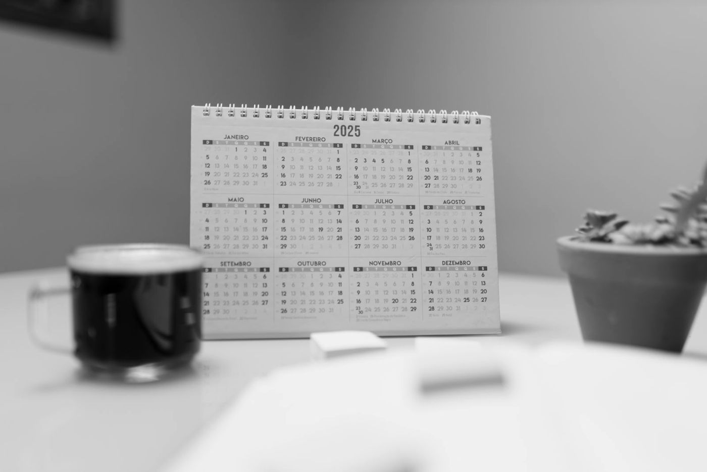 Calendário de mesa ao lado de uma xícara de café, em preto e branco