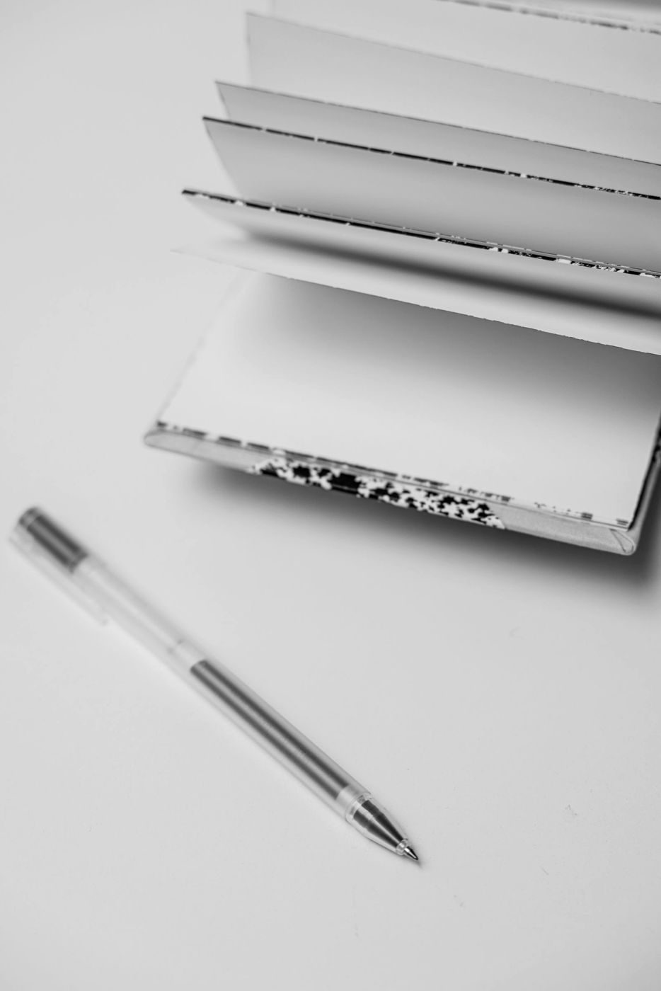 Caneta ao lado de um caderno aberto, em preto e branco