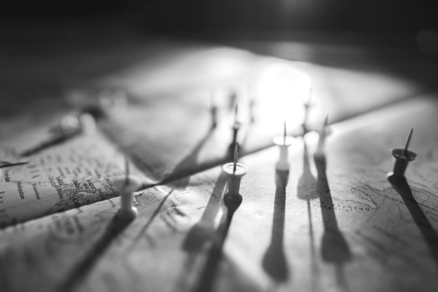 Alfinetes espetados num mapa, projetando sombras, em preto e branco